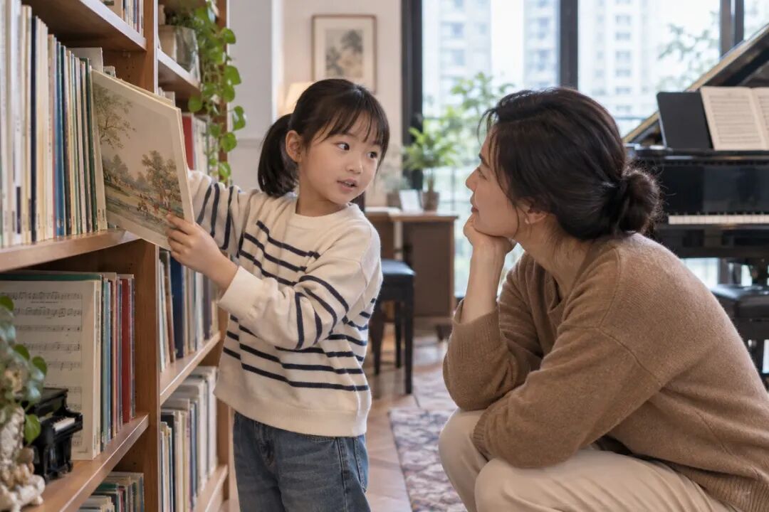 A child choosing sheet music they like in front of a bookshelf, while an adult crouches to the same height to listen. The scene is about making a choice rather than taking a lesson, with no phone visible.